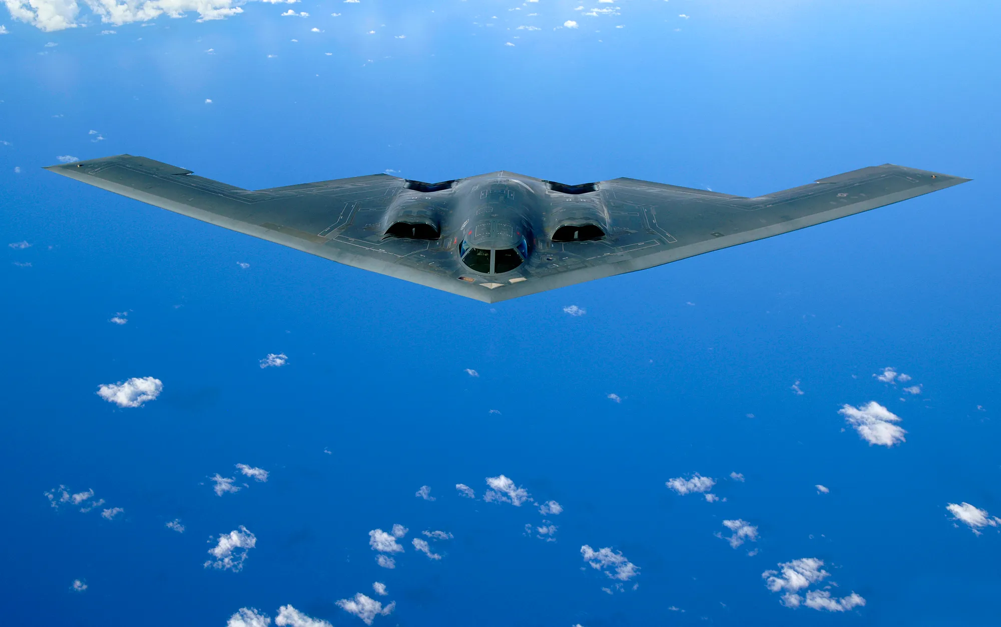 A B-2 Spirit bomber banking against a blue sky, seen from below