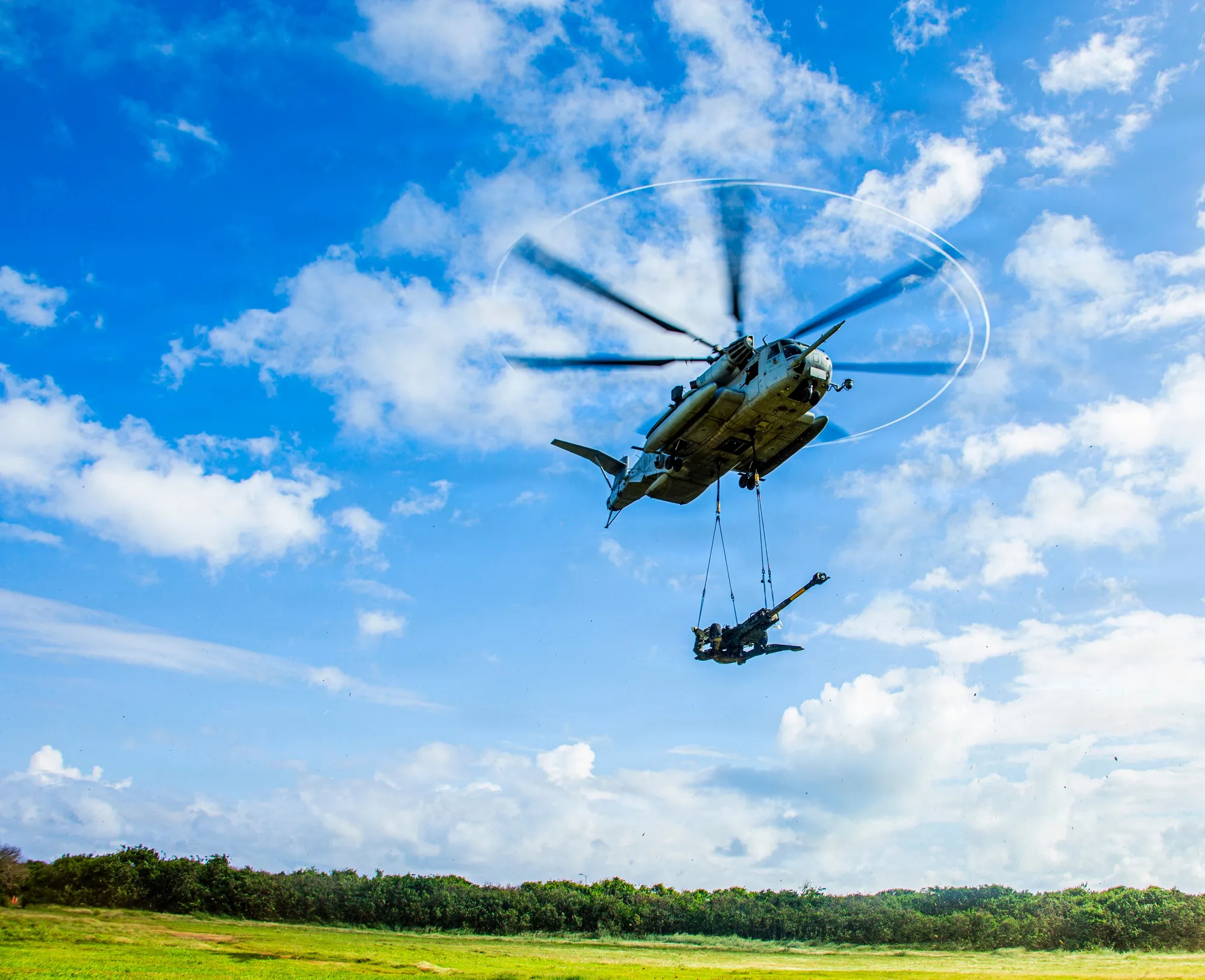 A Marine Corps helicopter lifting an M777 howitzer by sling load over Marine Corps Base Hawaii